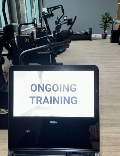 Fitnessstudio-Szene mit Trainingsgeräten und Bildschirm ONGOING TRAINING.
